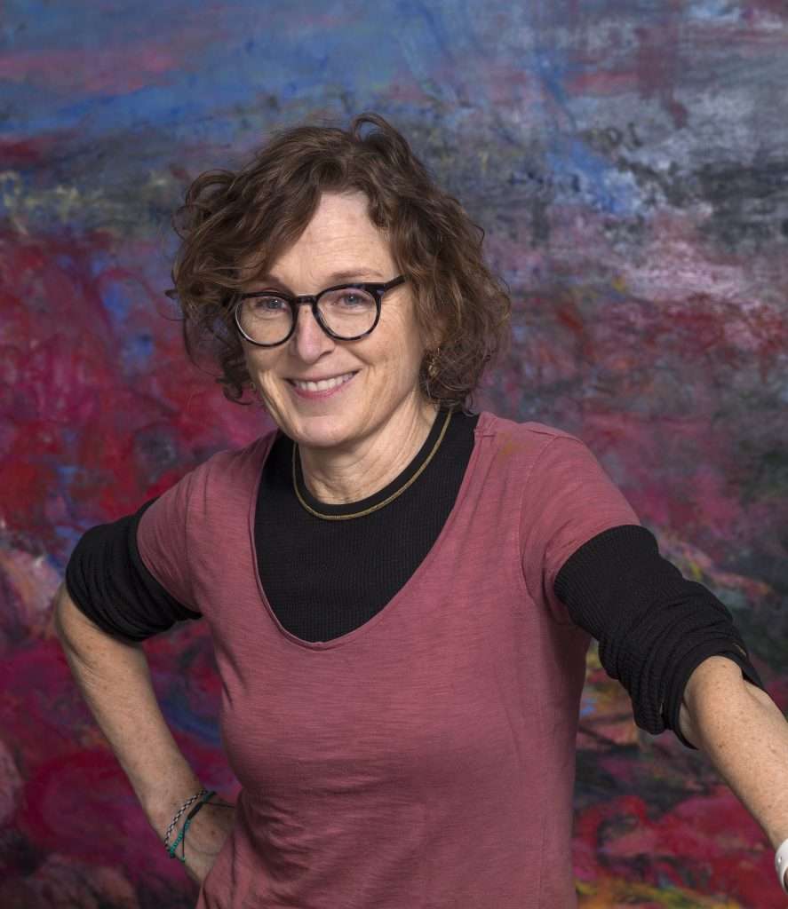 Ritratto dell’artista Helen O’Toole, sorridente su uno sfondo dalle sfumature viola e blu.