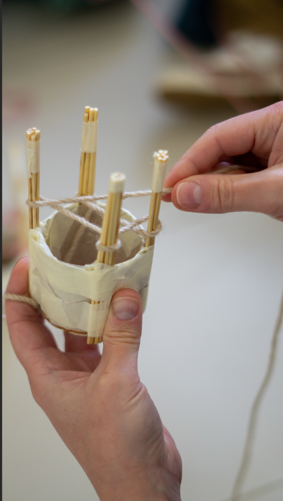 Un dettaglio del laboratorio Moving Thread di Paola Anziché: le mani di una persona intrecciano una sottile corda tra le parti lignee di un piccolo telaio manuale.
