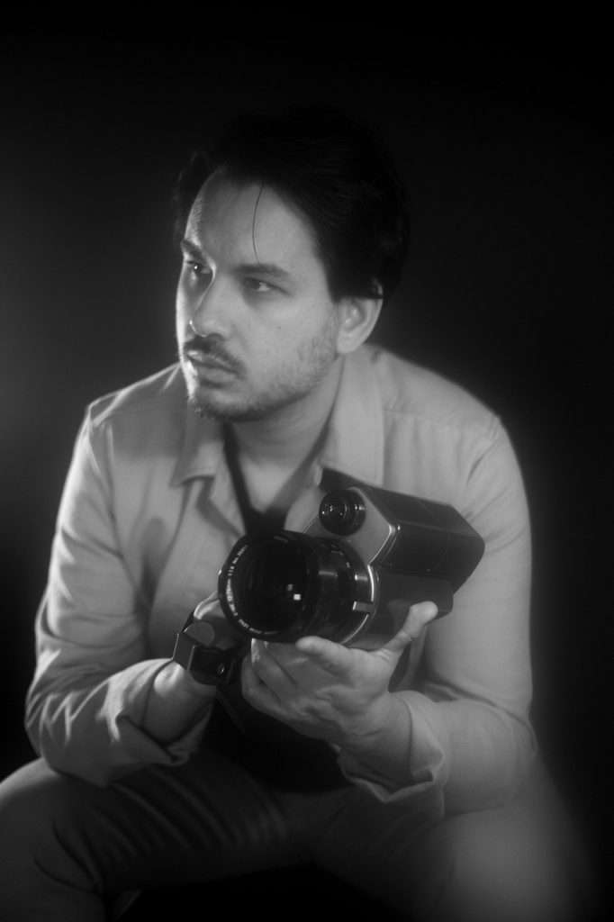 Close up image, black and white, of Suneil Sanzgiri with a camera
